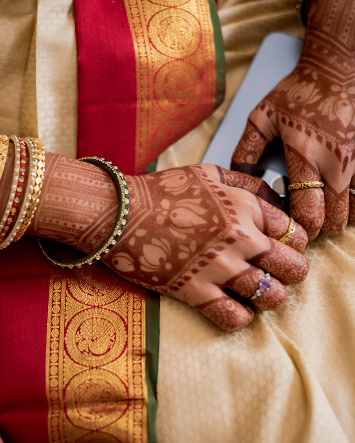 Mehndi-covered hands resting on gold silk, bangles catching the light