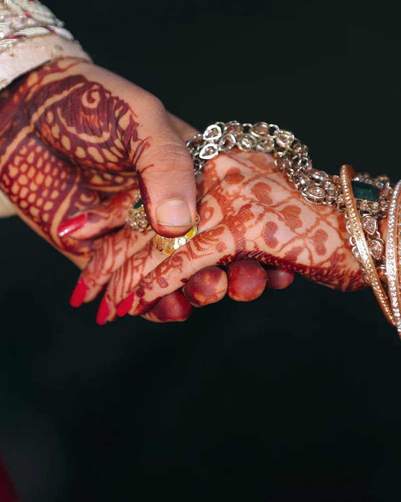 Bride's and groom's hands joined, her mehndi and red bridal chura in warm light